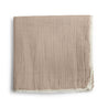 A taupe organic cotton muslin blanket with natural lace edges, neatly folded and placed on a white background. the fabric has a subtle striped texture by Makemake Organics.