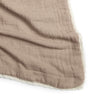 A close-up image of a crumpled taupe organic cotton muslin blanket with a delicate natural lace trim along the edge, displayed on a white background by Makemake Organics.