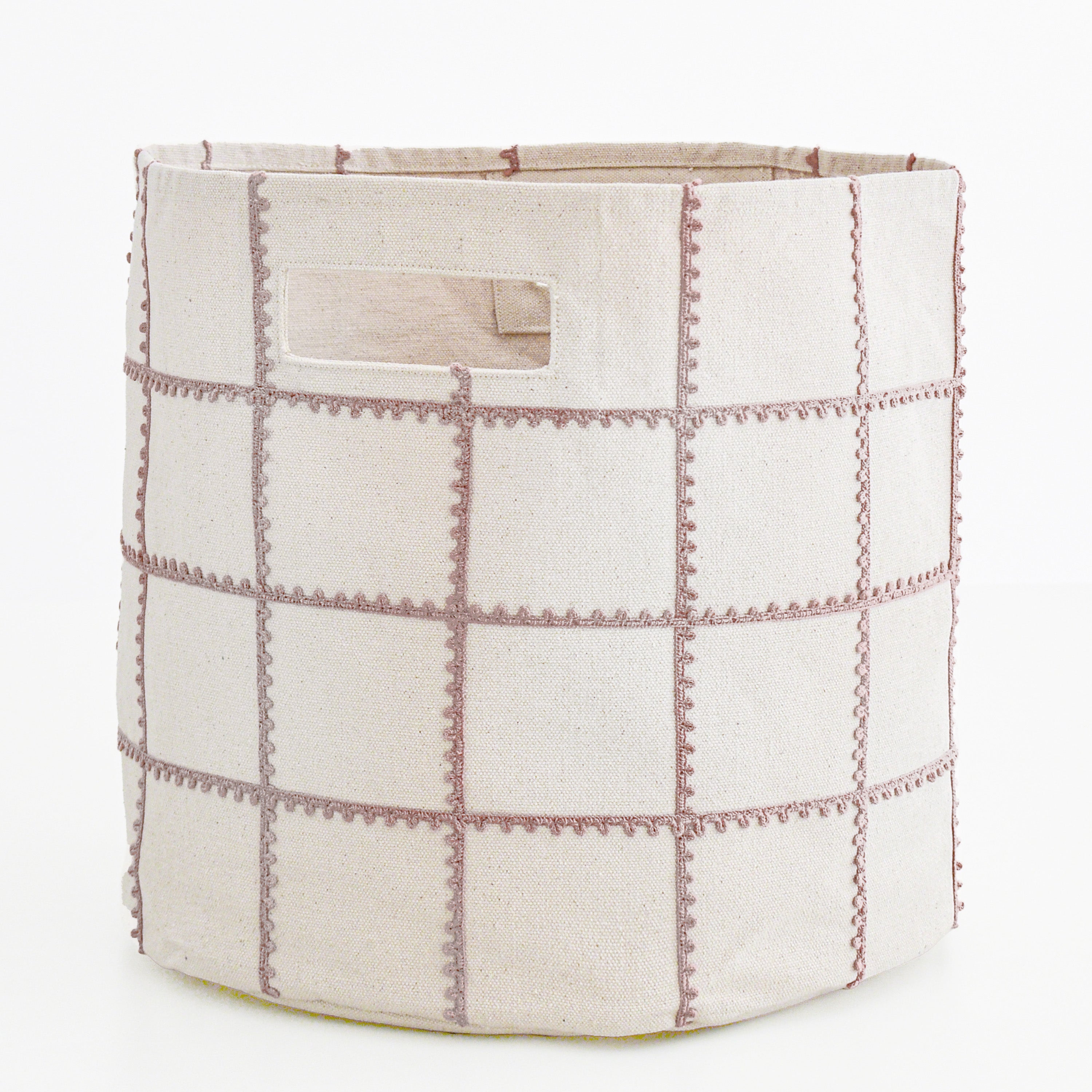 A beige Makemake Organics storage basket with a patchwork design and pink stitched details, featuring a small rectangular label on one side. the basket is set against a white background.
