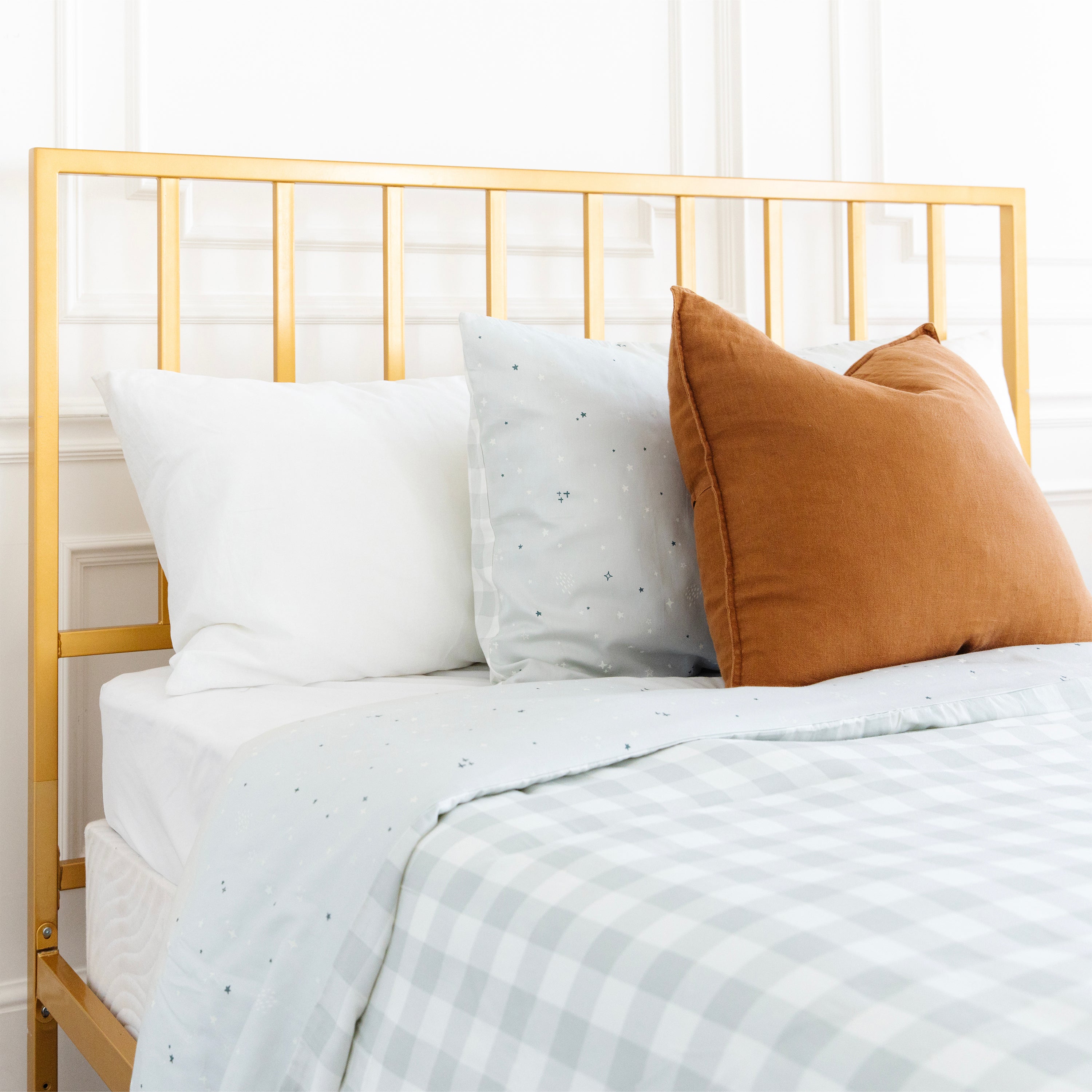 A neatly made bed with a gold-colored metal frame, featuring the Organic Duvet Cover - Milkyway & Gingham from Makemake Organics, complemented by white and brown pillows.