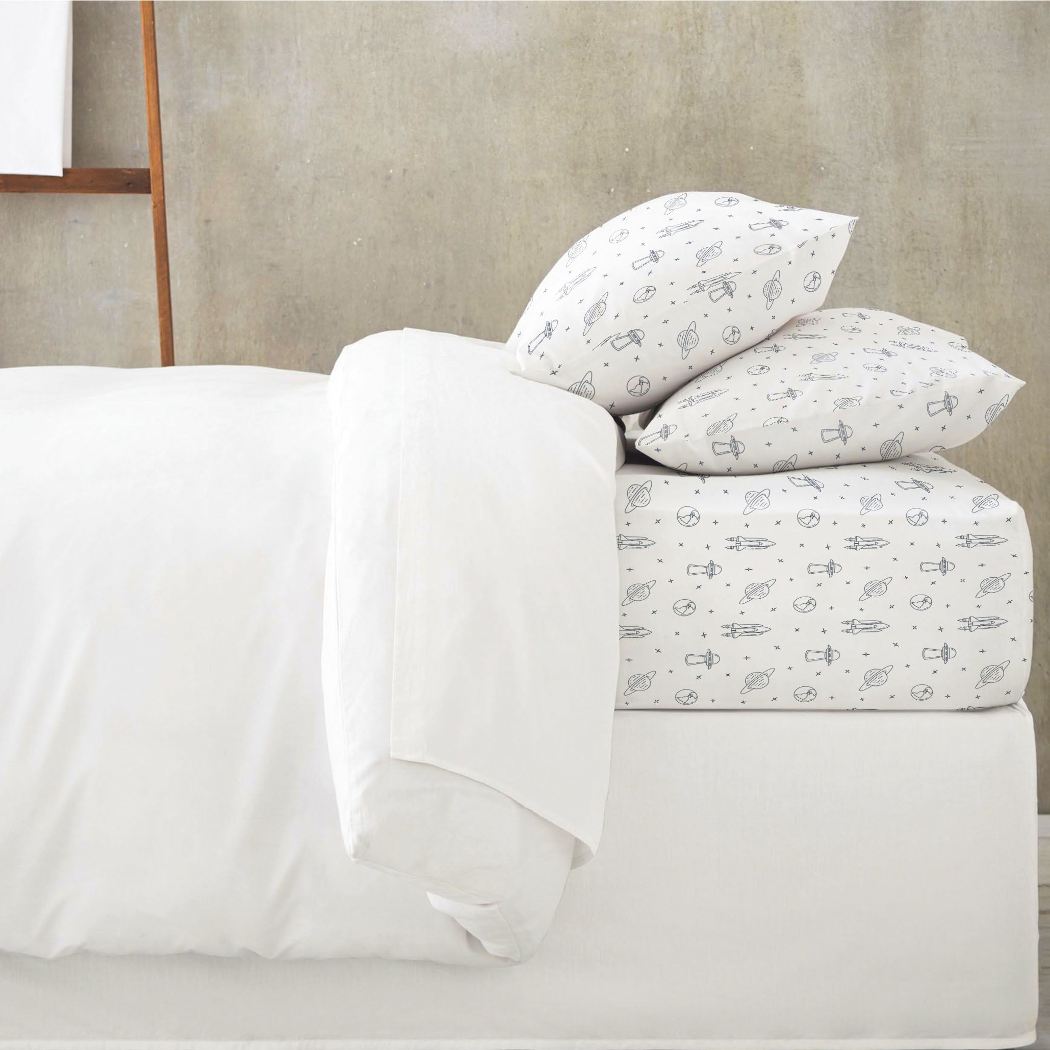 A neatly made bed with white sheets and pillowcases featuring a playful pattern of small, abstract designs, set against a soft gray background using the Organic Cotton Fitted Sheet Set - Celestial by Makemake Organics.