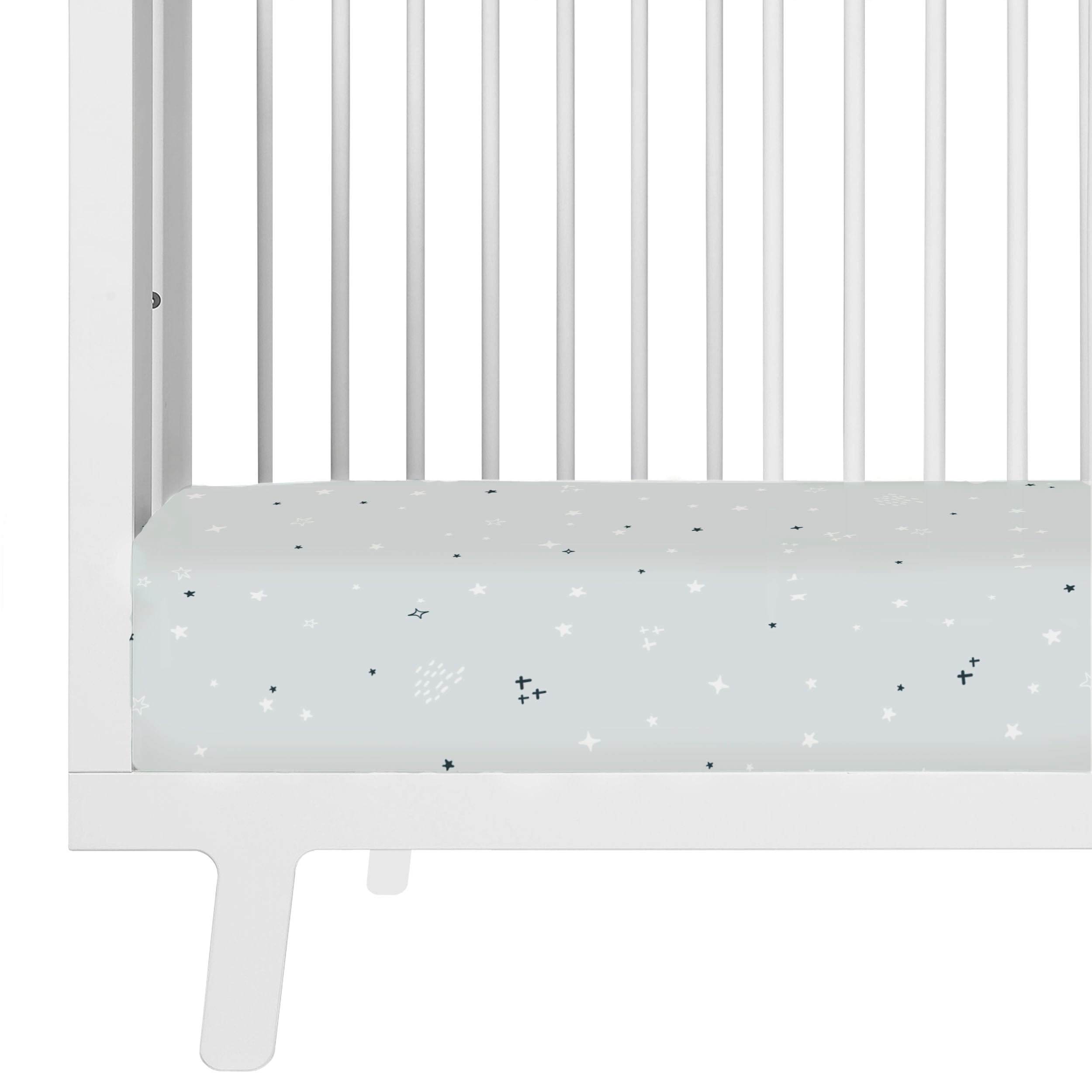 A close-up view of a white baby crib with a mattress covered in a Crib Fitted Sheet with Pillowcase - Milky Way adorned with a pattern of stars and small shapes from Makemake Organics.