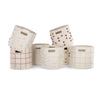 A collection of five Makemake Organics Storage Basket Pompom Taupe bins in various shapes, each adorned with unique patterns of textures and soft, neutral colors on a white background.