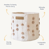 A round, sturdy canvas Makemake Organics Storage Basket Pompom Taupe with cut-out handles, adorned with decorative pom-poms, and labeled features like "ethically made" and "collapsible fabric.