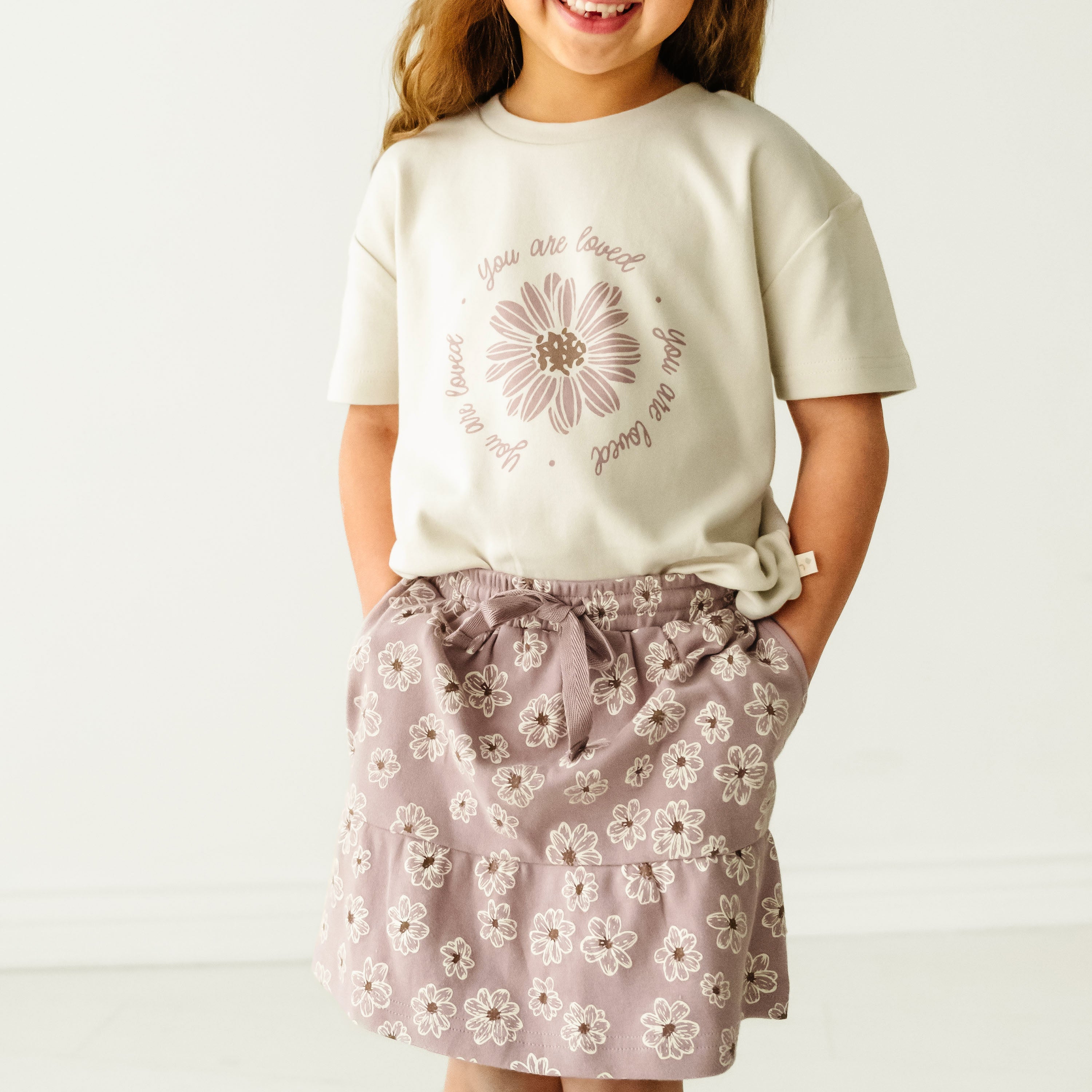 A young girl dressed in a Boxy Tee and Skort Set - Daisies from Organic Girls, standing against a plain background.
