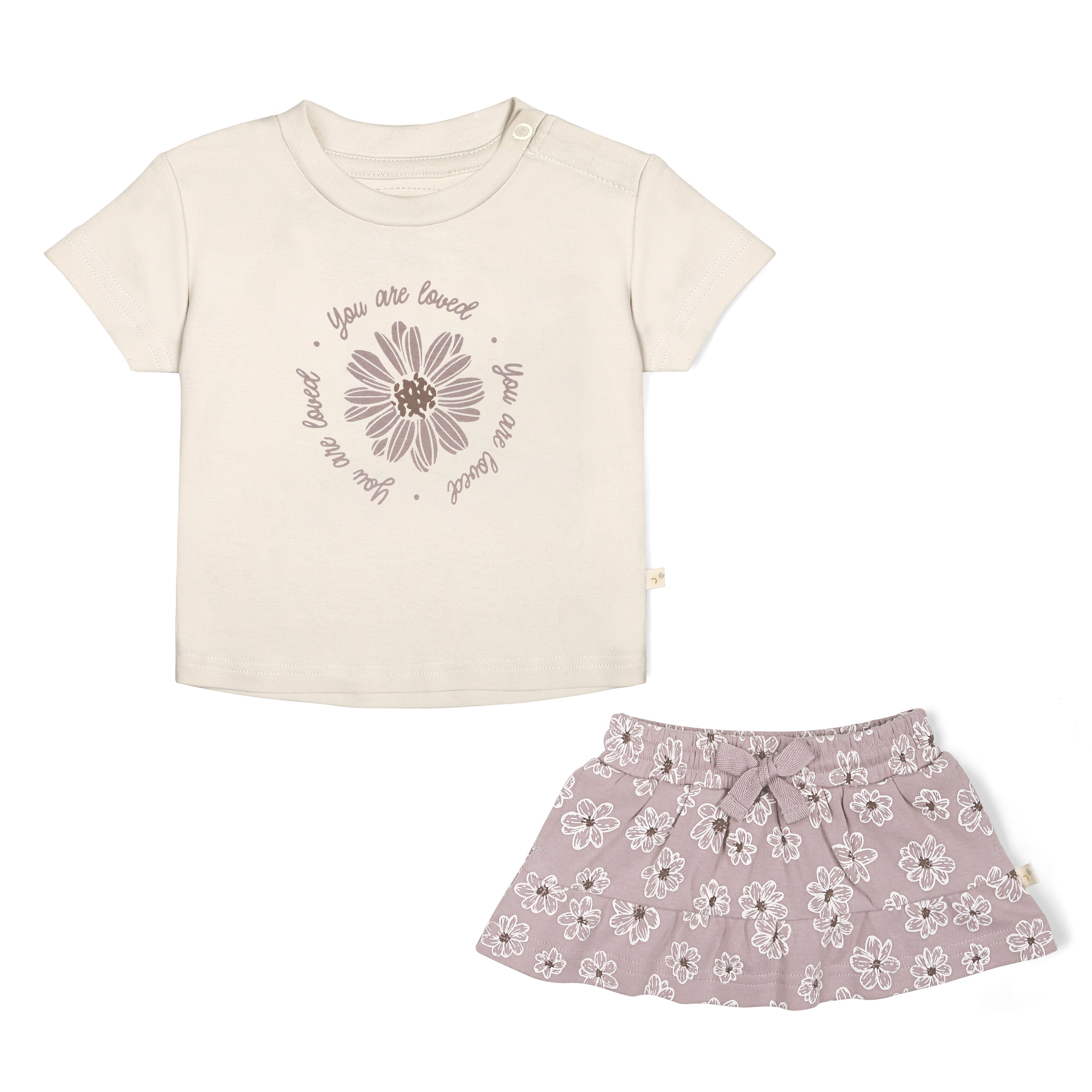 A light beige toddler Boxy Tee and Skort Set - Daisies with the phrase "you are loved" and a flower design paired with a gray floral print skirt, photographed on a white background by Organic Girls.
