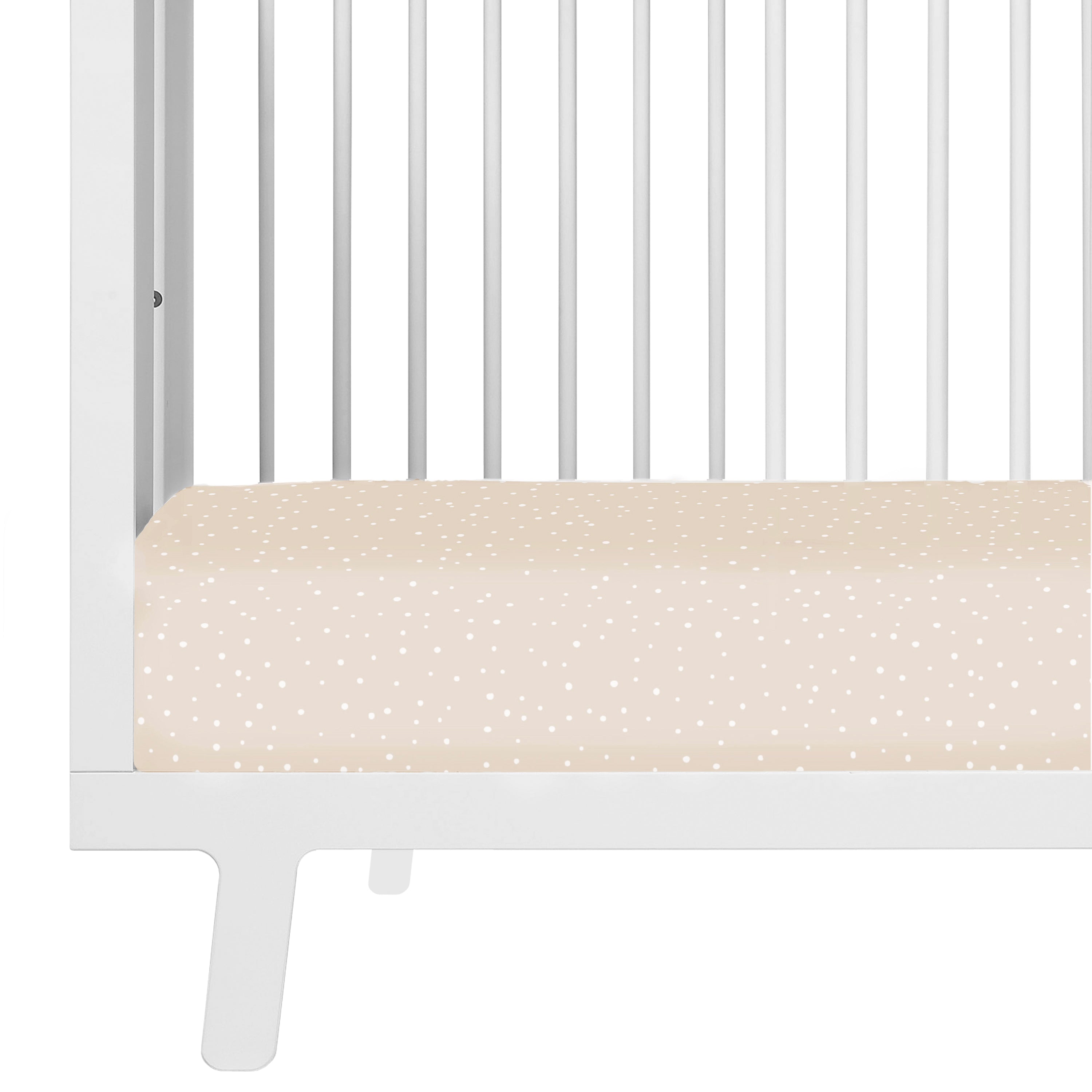 A close-up of a white Makemake Organics baby crib with a beige mattress featuring small white polka dots. The crib has vertical bars and a visible leg with a simple design.