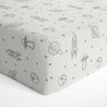 A Celestial Crib Fitted Sheet with Pillowcase from Makemake Organics, featuring various stylized drawings of planets, stars, rockets, and spaceships in black on a light gray background.