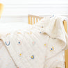 A cozy children's room featuring a Makemake Organics yellow crib with an Organic Cotton Comforter - Dotty & Rainbow draped over the side.