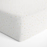 Close-up view of a Makemake Organics Crib Fitted Sheet with Pillowcase - Dotty decorated with small, colorful speckles. the image showcases the fabric texture and the neat seam along the corner.