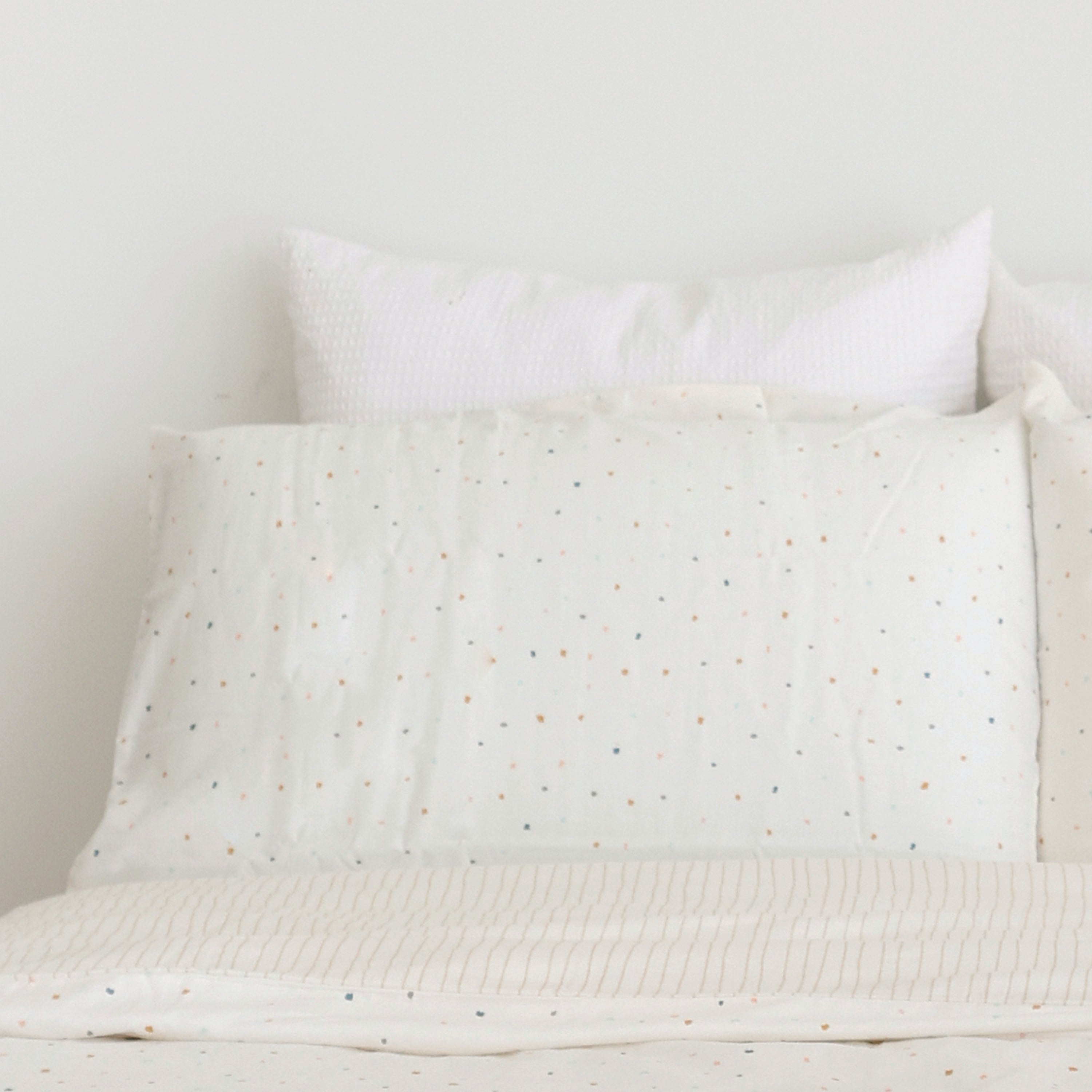 A neatly made double bed with white and polka dot bedding against a plain wall, showcasing two pillows and a clean, tranquil vibe with the Organic Cotton Toddler Pillowcase - Dotty from Makemake Organics.
