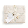 A neatly wrapped beige gift with a ribbon, featuring a tag labeled "Makemake Organics" and decorated with subtle floral patterns and polka dots, containing an Organic Cotton Pointelle Baby Blanket in Vanilla Natural.