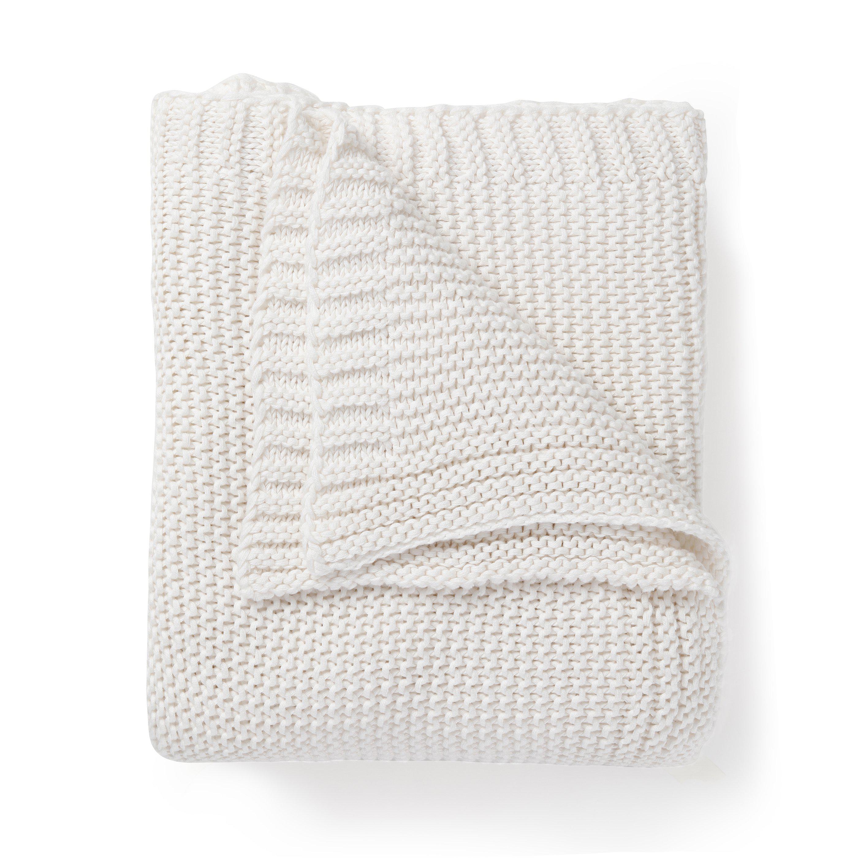A neatly folded Ella Ivory Chunky Knit Throw Blanket from Makemake Organics isolated on a white background, showcasing its textured, ribbed pattern.