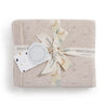 Beige Organic Cotton Pointelle Baby Blanket - Nora Shell neatly folded and tied with a ribbon, featuring a circular "Makemake Organics" tag and a decorative pattern of small circles and dashes.