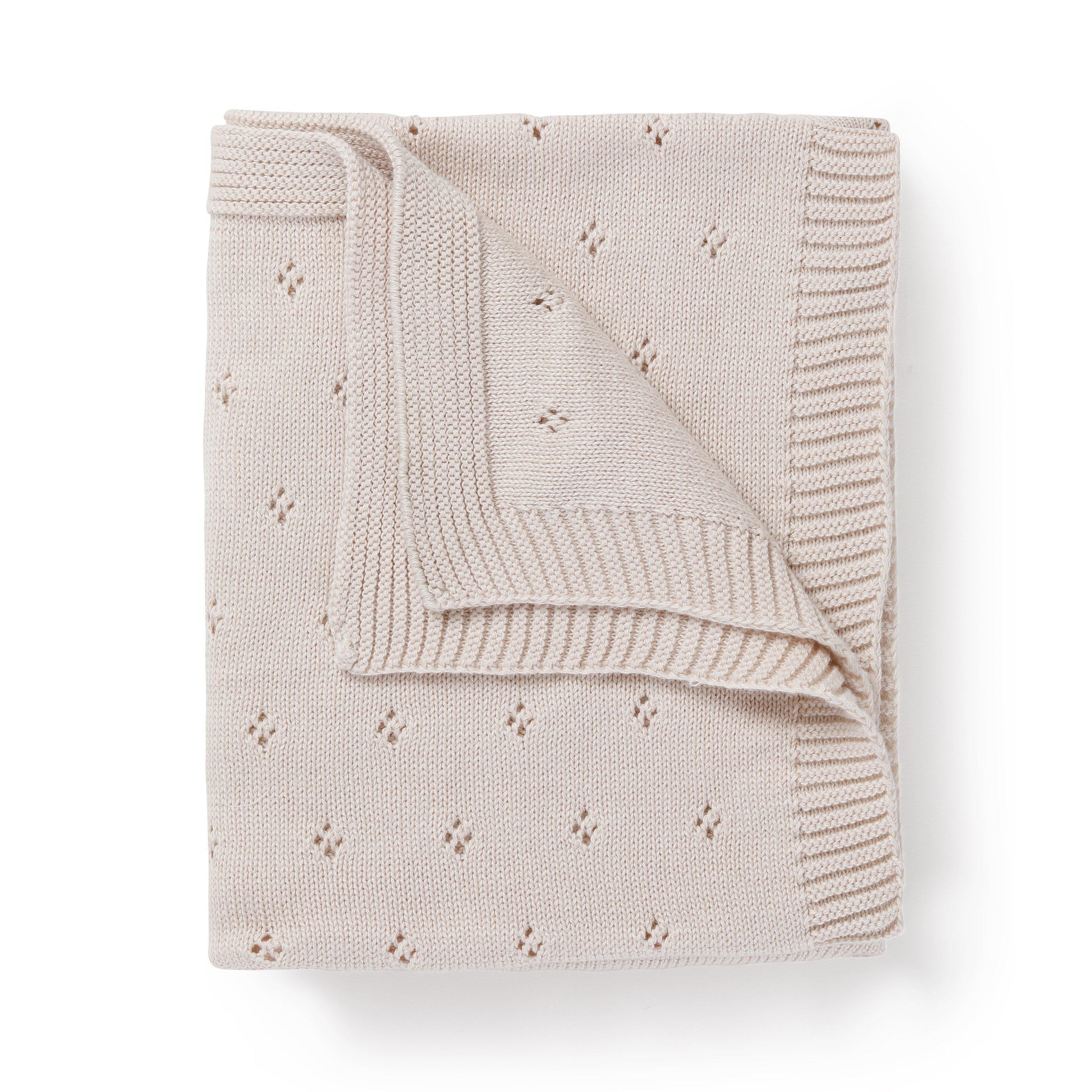 A folded Organic Cotton Pointelle Baby Blanket in Nora Shell with a delicate pattern of small diamonds and a ribbed border, isolated on a white background by Makemake Organics.