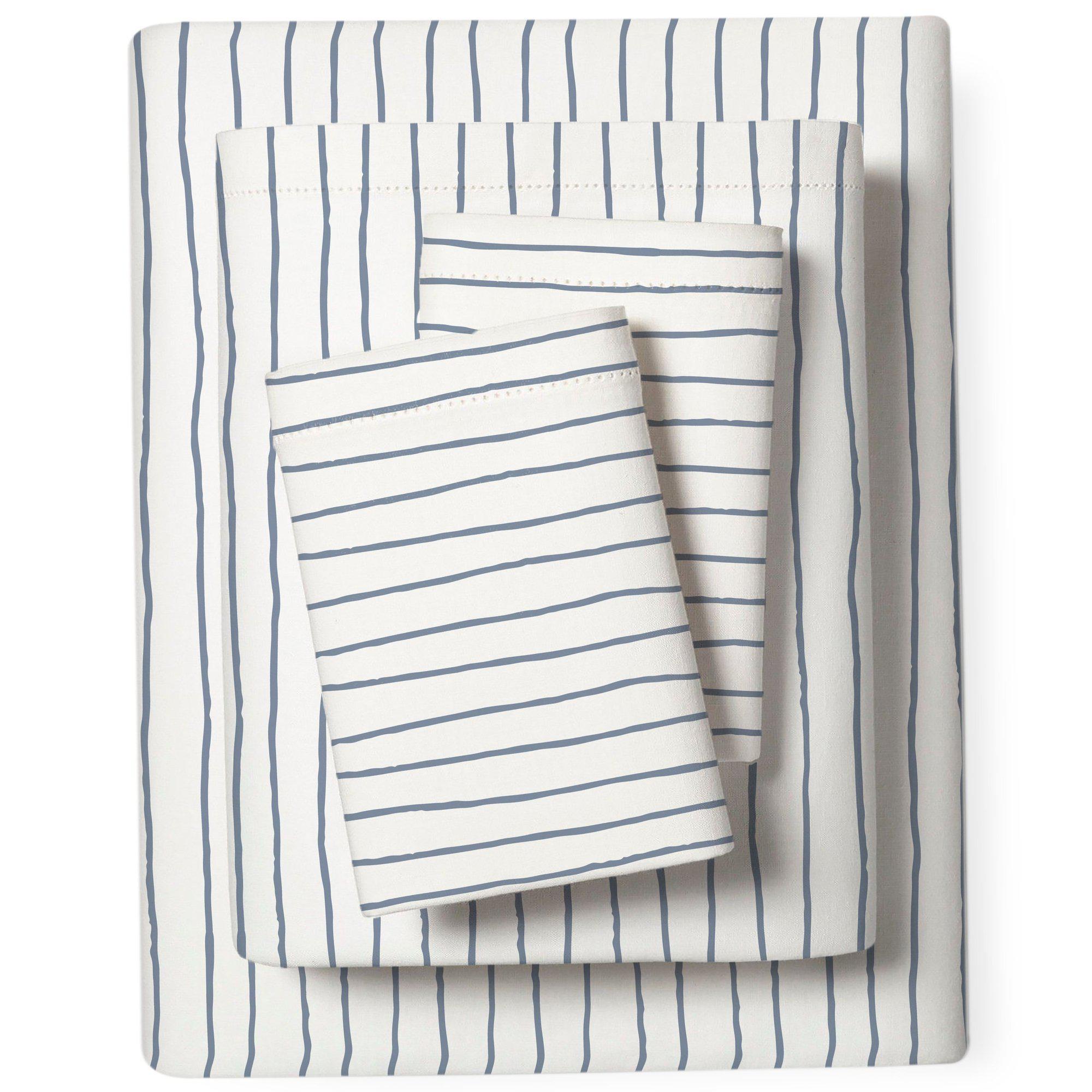 A white bedding set with navy blue stripes, including a folded duvet cover and a top sheet of the Organic Cotton Sheet Set - Cobi Blue Stripes by Makemake Organics, neatly arranged on a plain background.