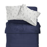A neatly made bed with a dark blue duvet and two pillows. The top pillow showcases a playful pattern with various space-themed drawings on a white background, featuring the Organic Cotton Toddler Pillowcase - Celestial from Makemake Organics.