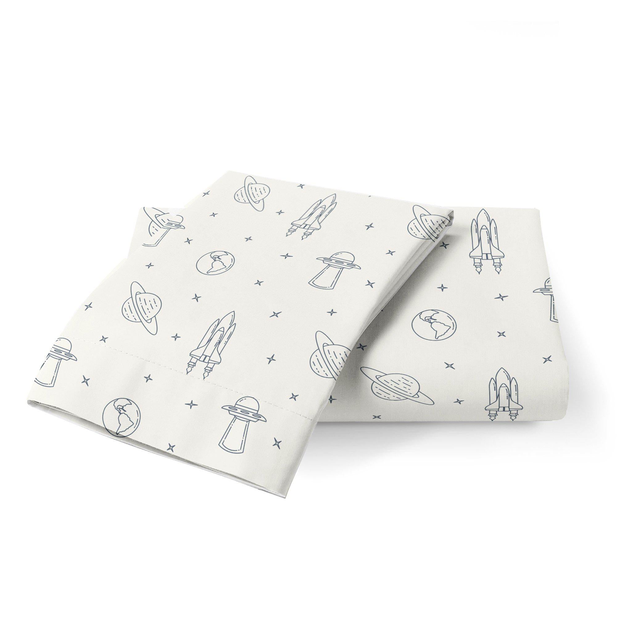 Two folded white towels with a blue space-themed pattern including rockets, planets, and stars, displayed on a plain white background of the Organic Cotton Toddler Pillowcase - Celestial by Makemake Organics.