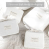 Eco-friendly gift packaging by Makemake Organics, featuring neatly tied cloth wraps around various sized boxes, all in a soft, natural white color, displayed on a textured bedsheet.