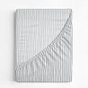 A closed notebook with a white cover featuring a black vertical striped pattern and a diagonal fold revealing a plain white underside from the Makemake Organics Crib Fitted Sheet With Pillowcase - Cobi Blue Stripes.