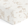 A close-up of a crib fitted sheet with pillowcase featuring a detailed animal and plant print in soft beige tones, including zebras, trees, and birds from Makemake Organics.