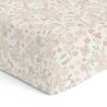 A Makemake Organics crib fitted sheet with pillowcase featuring a delicate floral pattern of pink and beige flowers with green leaves, draped over a surface, presenting a soft, inviting appearance.