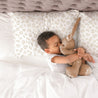 A young child gently hugs a stuffed rabbit while lying in a bed with heart-patterned sheets, conveying a sense of peace and affection on an Organic Cotton Toddler Pillowcase from Makemake Organics.