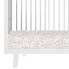 Close-up view of a white Makemake Organics crib with vertical bars, showcasing a Blossom floral patterned mattress with pastel pink and green colors.