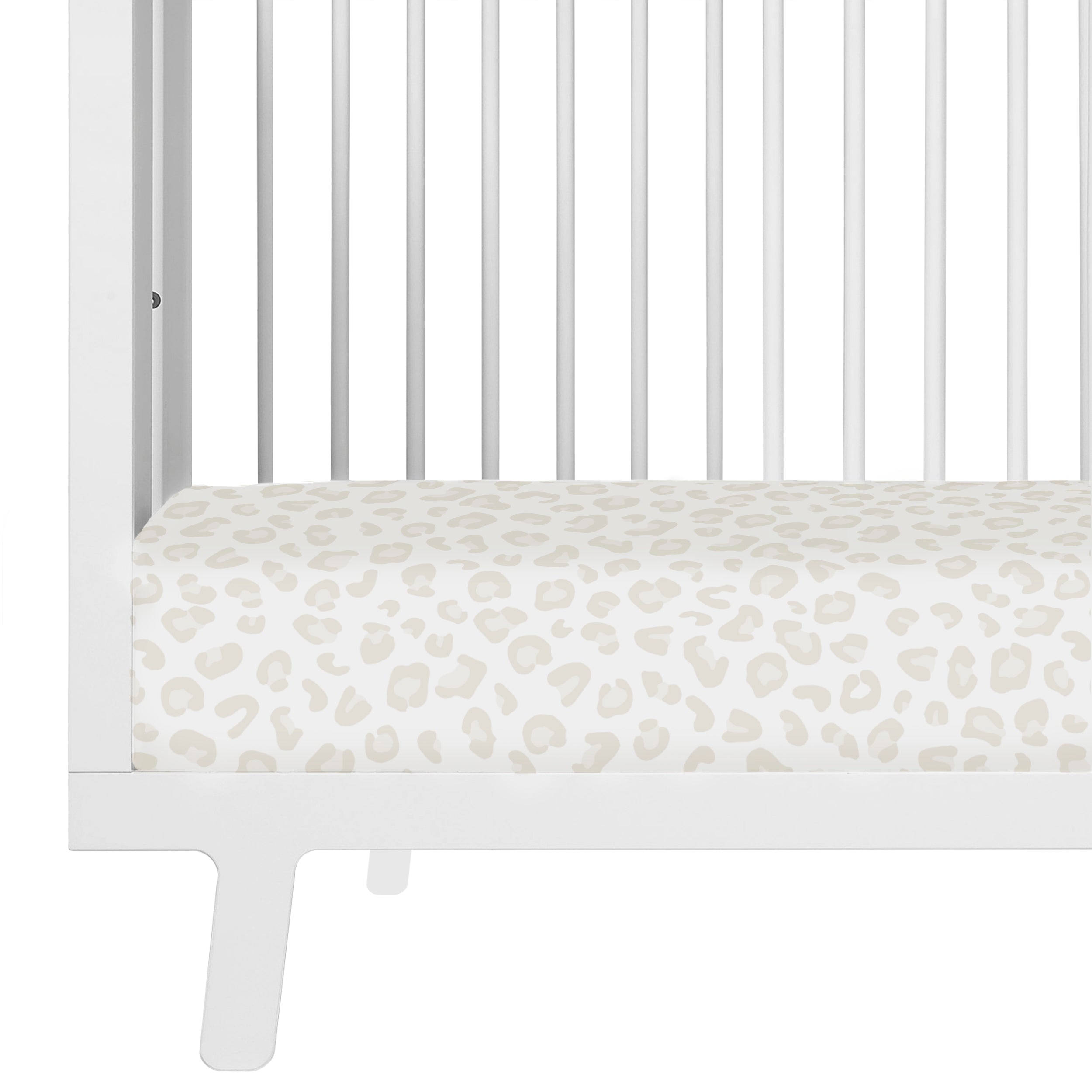 Close-up of a Makemake Organics white crib with a mattress covered in a Wild leopard print design. The crib features vertical bars and a visible side rail.
