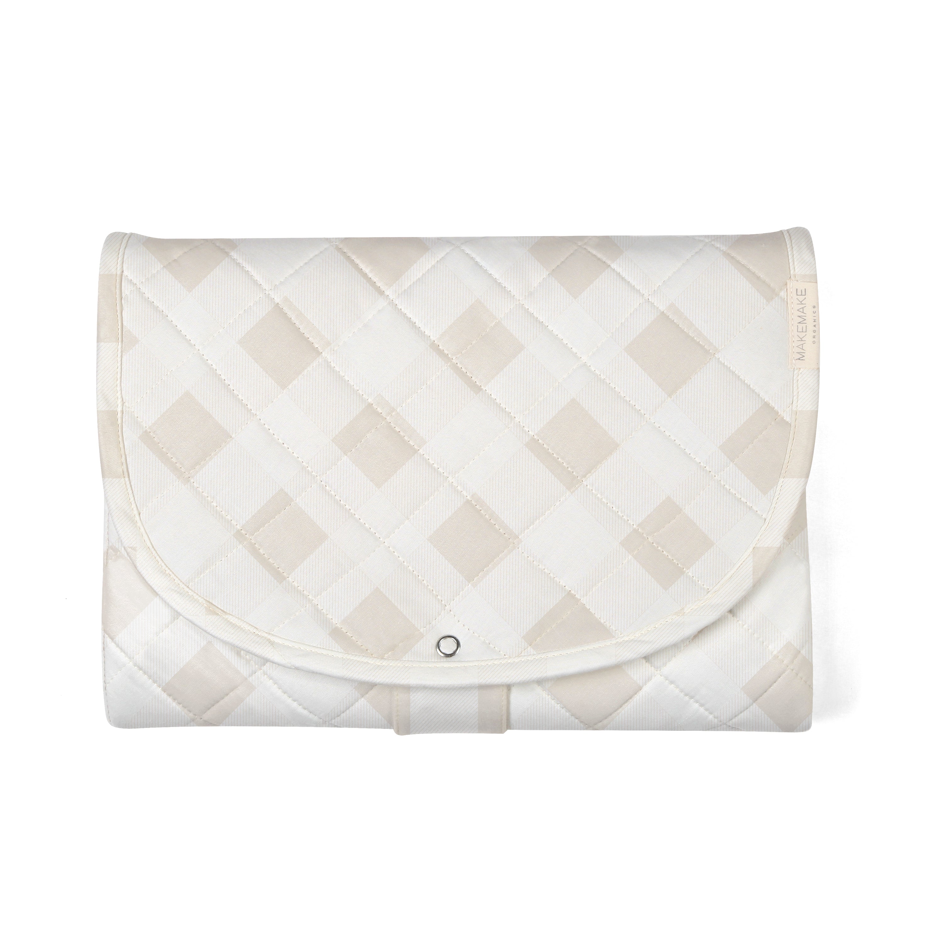 A light beige saddle pad featuring a quilted diamond pattern with a subtle Makemake Organics brand label and a black snap button closure, displayed on a white background.