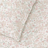 Two pieces of fabric with a floral pattern in soft pink, green, and cream hues, one piece slightly folded over the other, showcasing the design continuity of the Makemake Organics Organic Cotton Fitted Sheet Set - Blossom.