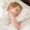 A young child sleeps peacefully on a bed with Makemake Organics Organic Cotton Toddler Pillowcase - Safari, resting comfortably with arms tucked under a pillow.