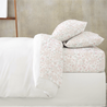 A neatly made bed with Makemake Organics Organic Cotton Sheet Set - Blossom bedding and a duvet turned down, topped with floral patterned pillows and sheets against a grey wall background.