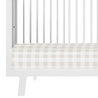 Close-up of a white Makemake Organics baby crib with a beige and white checkered Makemake Organics mattress. the crib features vertical slats and a sturdy frame.