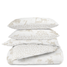 Three neatly stacked pillows and a folded Organic Duvet Cover - Safari & Wild from Makemake Organics, featuring zebras, giraffes, and foliage in a subtle beige tone against a white background.