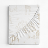 A journal with a textured cover featuring a serene african savannah theme, including illustrated giraffes, trees, and birds, partially obscured by a diagonal fabric flap.
