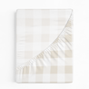 A folded beige and white checkered Makemake Organics Crib Fitted Sheet with Pillowcase, with the corner flipped over, showing the plain white underside, isolated on a white background.