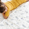 A child in a yellow shirt lying face down on a bed with Makemake Organics Organic Cotton Fitted Sheet Set - Celestial patterned with various space-themed drawings such as planets and rockets.