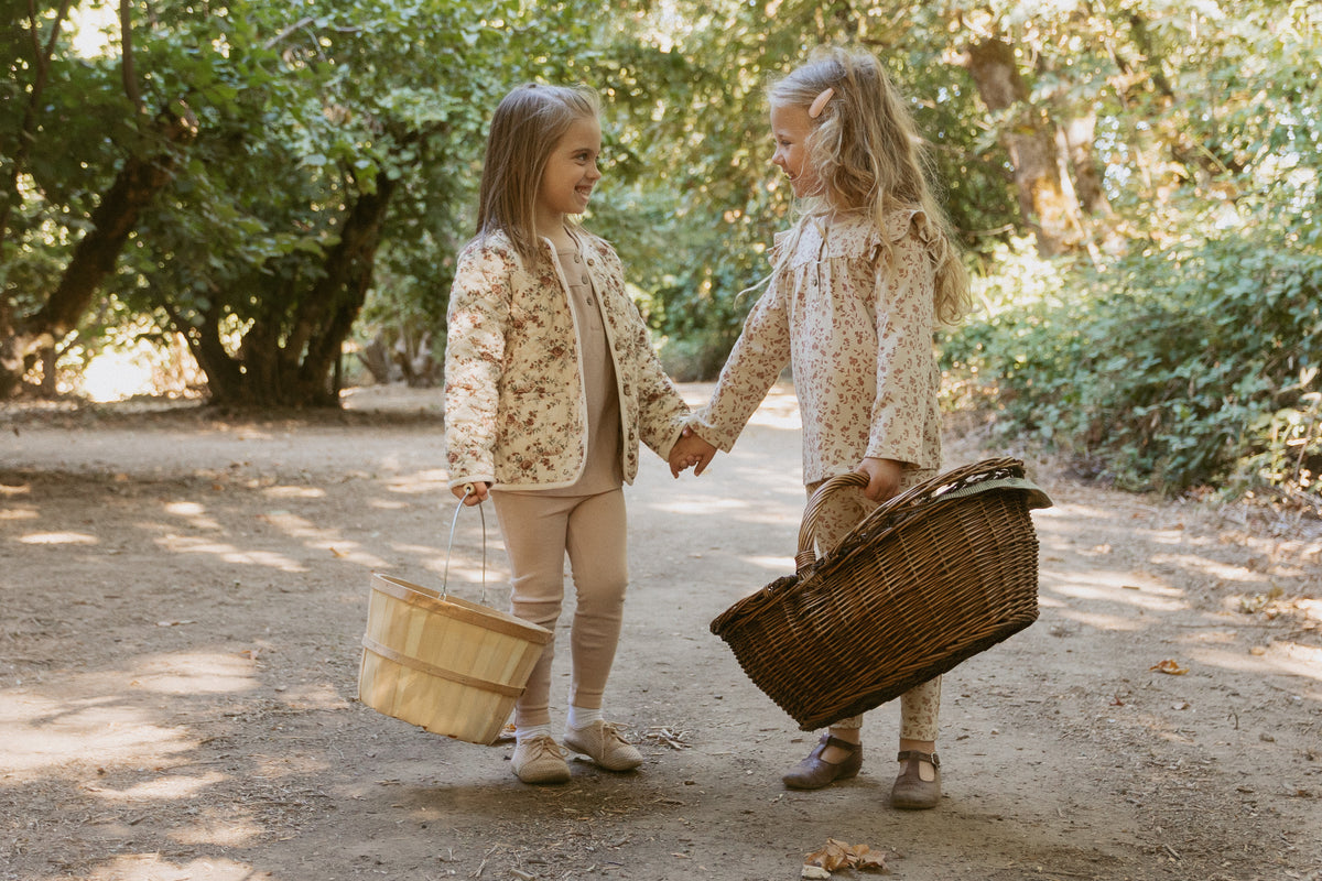 Two girls in floral quilted jackets holding hands on an orchard path