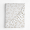 A folded beige Organic Cotton Sheet Set - Wild baby blanket from Makemake Organics with a leopard print pattern on a white background. the blanket has a smooth texture and ruffled edges.