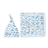 A baby's knotted beanie and square blanket set in white with a blue feather pattern, displayed on a white background. The blanket has a visible label that says "Organic Swaddle Blanket & Hat - Minnow" by Makemake Organics.
