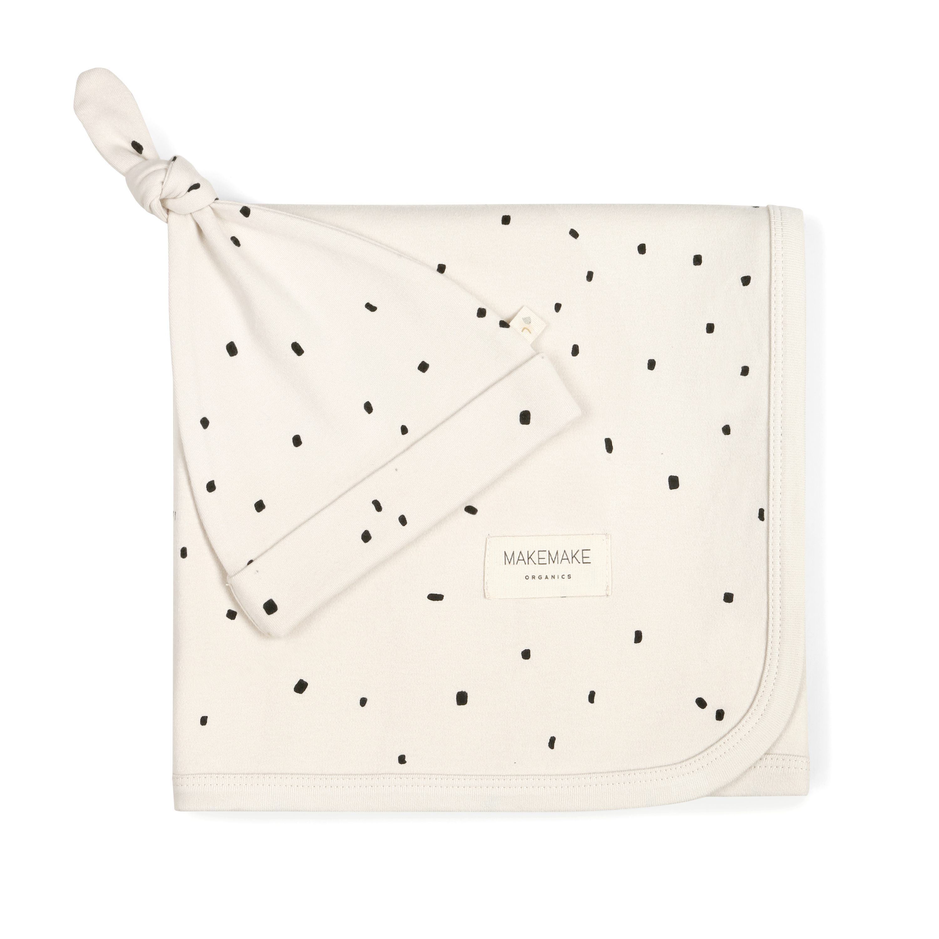 A cream-colored Makemake Organics swaddle blanket & hat neatly folded on a white background, decorated with a scattered black dot pattern, featuring a small visible logo.