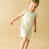 A young boy in Organic Kids Foam Stripes organic tee and shorts is playfully jumping, with a joyful expression, against a soft beige background.