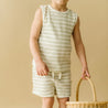 A child in Organic Kids' Foam Stripes tee and shorts holds a wicker basket against a plain beige background, conveying a warm, casual atmosphere.