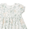 A Organic Kids Wild Safari baby dress with a tropical pattern featuring green foliage and beige giraffes, displayed on a white background. The dress has short ruffled sleeves and a gathered waist.