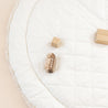 Overhead view of a Makemake Organics Organic Cotton Quilted Reversible Play Mat in Dotty and Ivory with three simple wooden toys, including a car and two blocks, arranged sparsely on it.