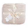 A neatly folded Nora Shell Chunky Knit Throw Blanket tied with a decorative ribbon and a gift tag, isolated on a white background. The tag and ribbon feature the brand "Makemake Organics.