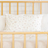 A cozy scene with a Makemake Organics Organic Cotton Toddler Pillowcase adorned with a delicate floral pattern on a bed, framed by a yellow metal headboard, against a soft, off-white background.