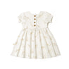 A white toddler dress from Organic Kids with a giraffe print, featuring short sleeves, a gathered waist, and a line of golden buttons down the front, isolated on a white background.