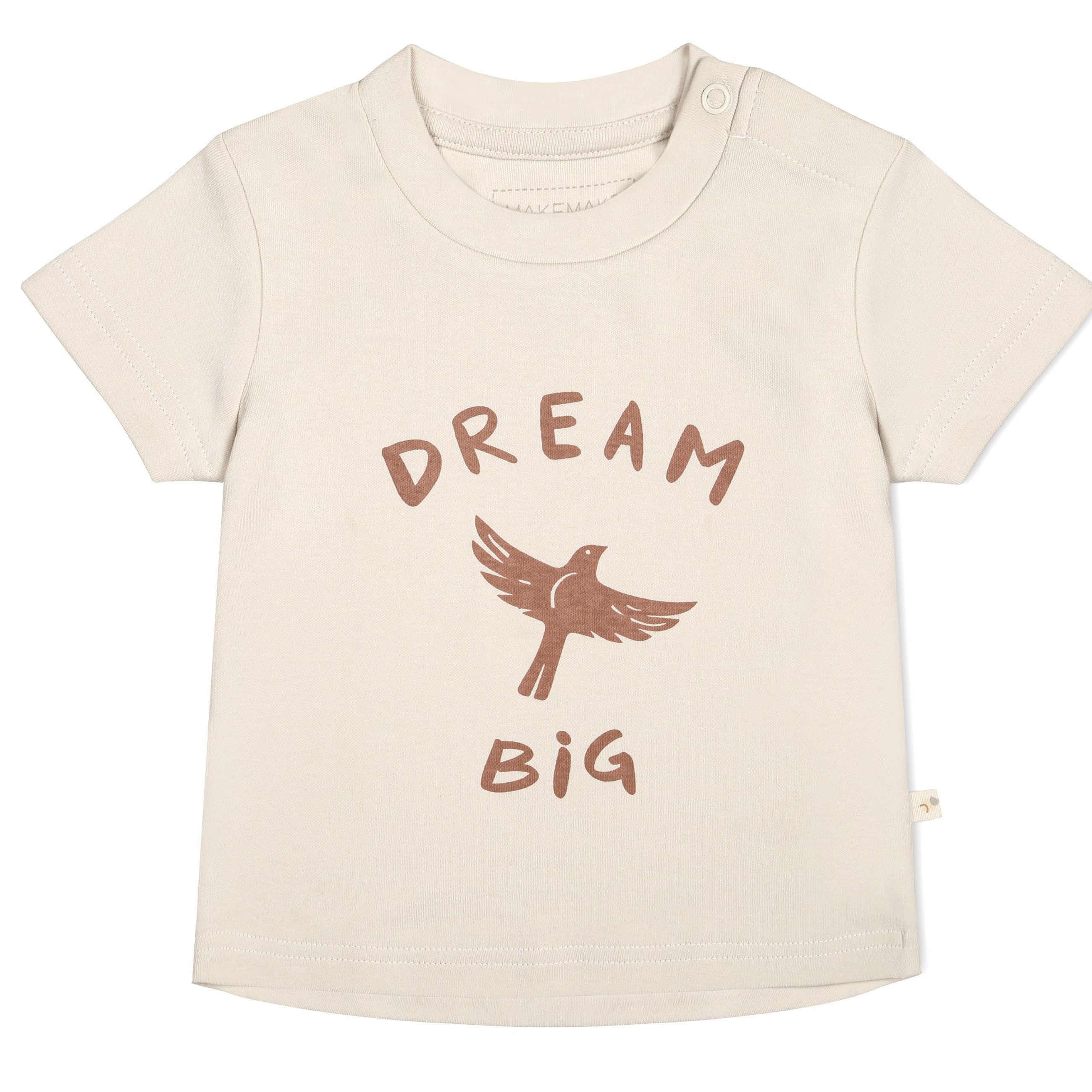 A cream-colored Makemake Organics Organic Crew Neck Tee with the phrase "dream big" in brown text, featuring an illustration of a bird in flight above the words. The shirt has a small button on the left shoulder.